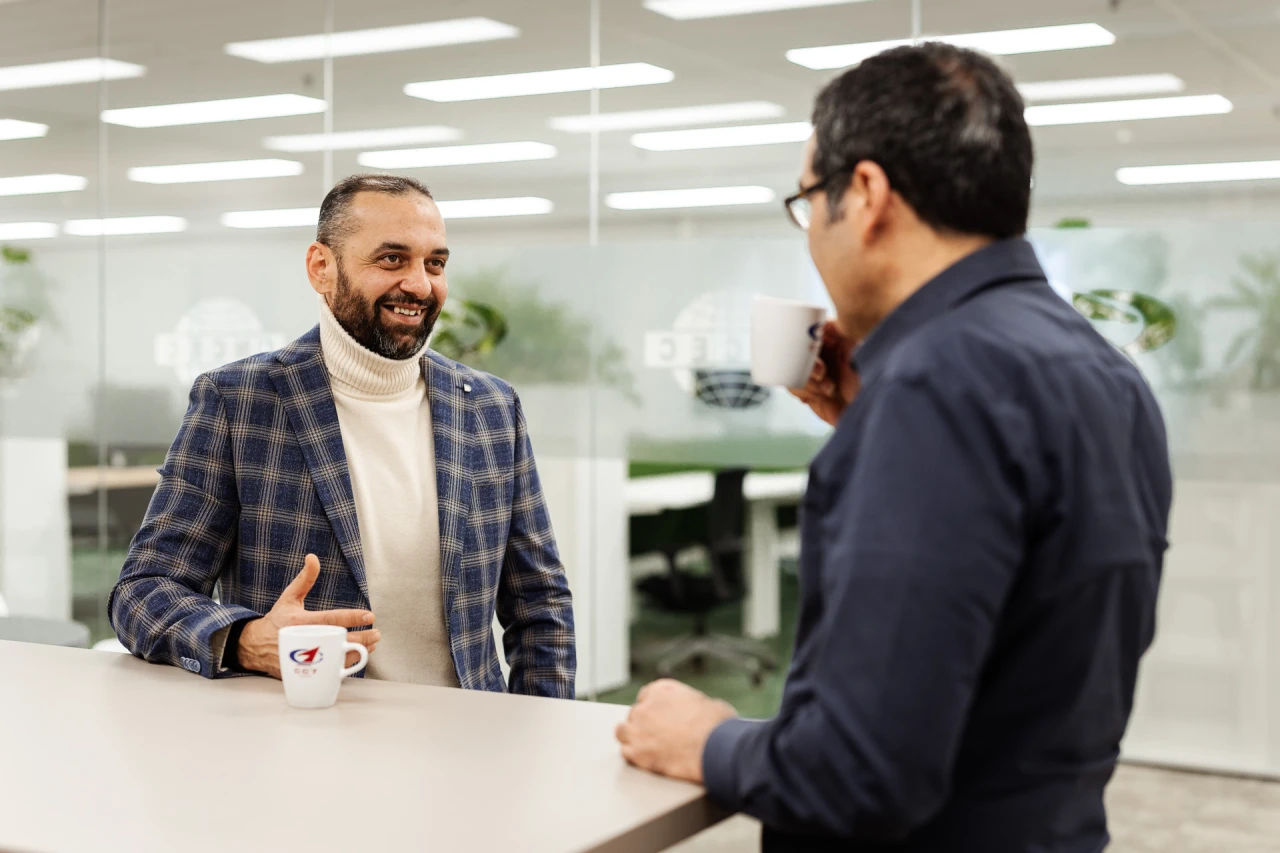 2 smiling men standing and talking while they drink from 2 cups. 2 smiling men standing and talking while they drink from 2 cups.