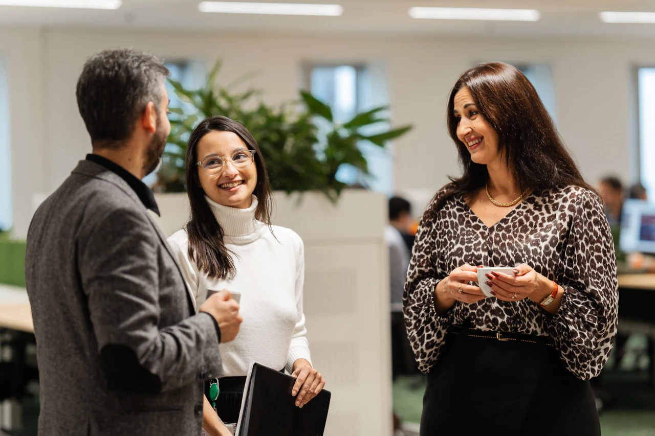 3 people standing and smile while conversing in office and holding 1 agenda and 1 cup. 3 people standing and smile while conversing in office and holding 1 agenda and 1 cup.